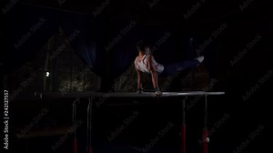 Male gymnast acrobat performs handstand on parallel bars in a dark room in slow motion sharing a somersault and landing on the floor. Training before the Olympic games. A professional athlete
