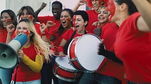 Crowd football fans exulting while watching soccer game at stadium - People with painted face and drum encouraging their team - Sport entertainment concept