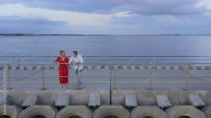 Couple converses by stunning causeway, red dress. Slo motion. Bay