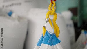 Close-up of yellow hook from crane cathead in the factory workshop, warehouse. Industrial hook gripping a white bulk bag. Rigging works, carrying goods, loading materials to the train for delivery