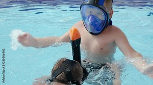 Two boys in underwater masks with snorkels play in the resort pool slow motion. Children have fun in the pool. Active summer vacation at the resort