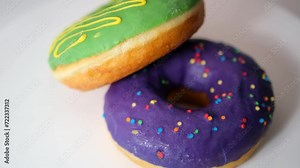 Two fresh - green and lilac donuts rotate on a platform on a white background.