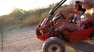 Young girls go on dune buggy on dirt road enjoying extreme rest. Riding along sandy road on beach buggy. Girls driving dune buggy. Extreme trip on earth road. Extreme vacation ride