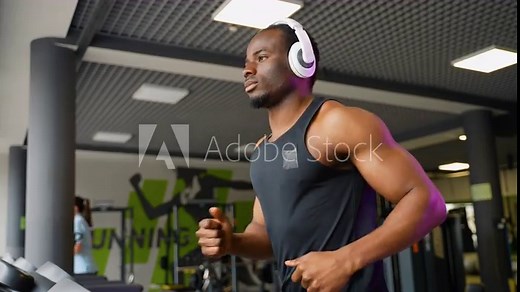 A man with headphones running in a modern gym on a treadmill
