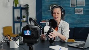 Tech enthusiast presenting VR wearable headset specifications to audience while recording video in living room studio. Vlogger sitting at desk while reviewing futuristic virtual reality goggles.