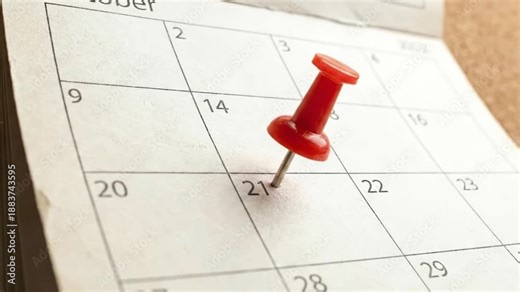 Close-up of red push pin marking the 21st of October on a paper calendar for deadline and scheduling concepts