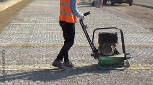 Workers using a vibro-compacting plate to compact self-locking blocks in their laying bed