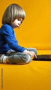 A small child counts on a calculator on a yellow background. Kid fingers press buttons and calculate studying math at home. Child makes arithmetic calculations with a calculator