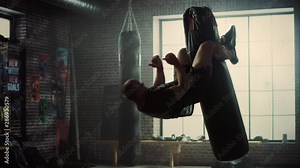 Insane Punching Bag Crunches. Strong Masculine Man Embrassing the Bag with His Legs and Pumping His Abs and Core Muscles. Handsome Male Trains in a Gym with Motivational Posters.