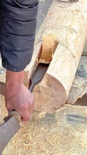 chiseling a thick wooden log manually to create a large hole for building traditional structures