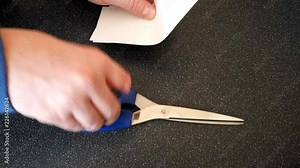 Male with a partially amputated index finger on his right hand cutting strips of white paper diagonally with a pair of blue handled scissor#orrs