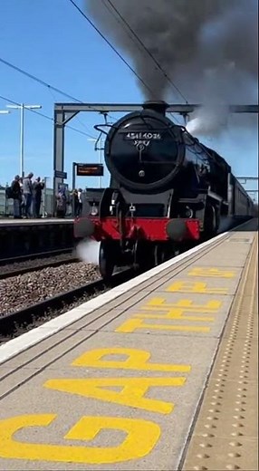A vintage steam locomotive emerges from the distance, billowing thick white smoke