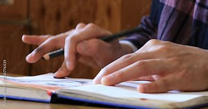 Asian young man drawing on notebook page with color pencils