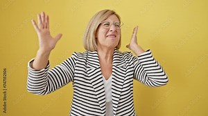 Cheerful, blonde, middle-aged woman in a striped jacket, ecstatically cheers her win! she's standing, exulting in victory, amidst a bright yellow isolated backdrop.