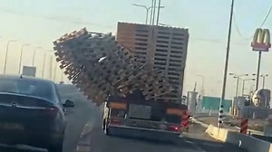 Stack of pallets lean precariously from back of moving truck