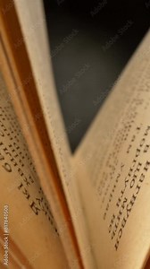 Camera moves through opened vintage book. Old book lying with their pages open. Black background. Slider vertical shot