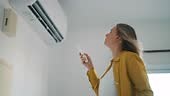 Woman holding remote control aimed at the air conditioner.
