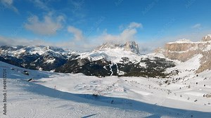 View of a ski resort piste with people skiing in Dolomites in Italy. Ski area Belvedere. Canazei, Italy. Horizontal camera pan