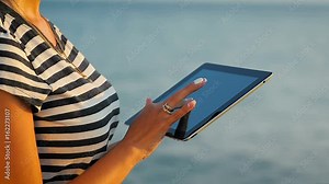 Close-up woman hand using tablet ipad in a trip by the sea.