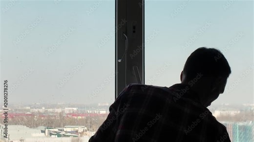 Professional cleaner wearing yellow gloves carefully washes a large window pane. Man doing household chores with a cityscape view outside