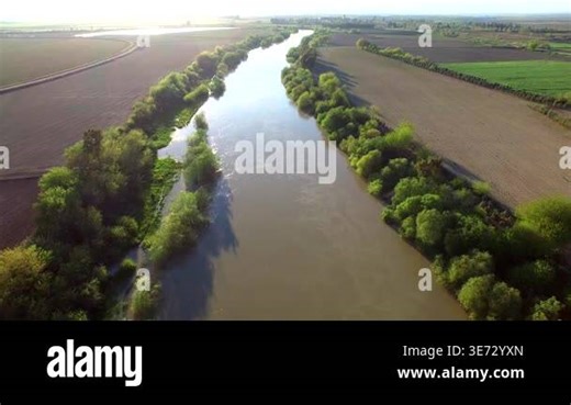 Aerial view of the Nile River flowing through African farmland with green banks and calm water. Vast cultivated plains surround the winding river creating serene and fertile landscape.