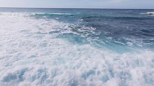 Serene aerial view of the North shore Pacific Ocean near Oahu, Hawaii, with vibrant blue waves rolling under a partly cloudy sky, showcasing a tranquil seascape.