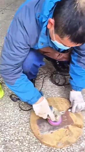 using a handheld electric angle grinder to polish the surface of a metal plate on a wooden base