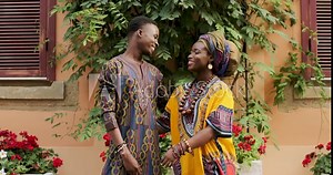 Portrait of the happy romantic African couple in love standing in the beautiful yard in traditional clothes, looking at each other and smiling to the camera while hugging.