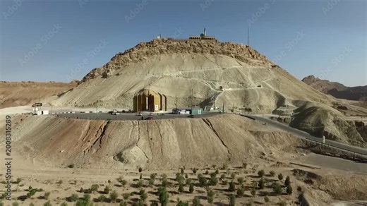 Wide aerial view of a conical desert hill with a shrine entrance carved into its base, capturing dramatic geology, religious significance, and the stark contrast between faith and terrain.
