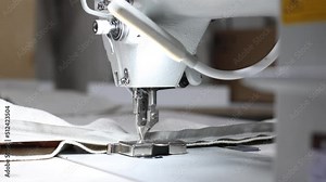 Sewing machine needle is in motion. Close-up of the sewing machine needle moves up and down quickly. Seamstress stitches beige fabric at sewing workshop. Process of sewing fabric. 4k slow motion video