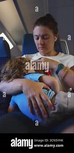 Mother breastfeeding toddler on train seat while comforting child during journey, candid parenting moment showing connection, tenderness, and care Stock Video Footage - Alamy