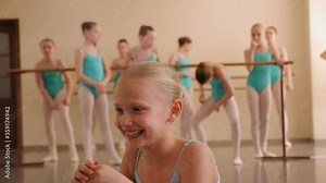 Close-up portrait of a little ballerina in a ballet school against the background of a rehearsal room with ballerinas near the ballet barre. Little girl dreams of becoming a ballerina.