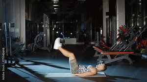Strong male athlete workout in gym doing sit up exercises lifting straight legs to his torso lying on floor mat