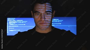 Developer hacker programmer working on computer in a data center while blue code characters reflect on his face in a dark office room.