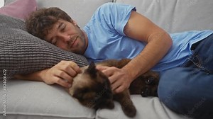 Casual hispanic man cuddling with a siamese cat on a gray sofa in a cozy living room