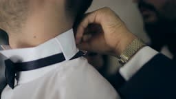 Groom getting dressed with the help of his best friend for his...