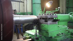 A metal round billet rotates in a lathe and is machined by a turning tool. Metal shavings fly off the workpiece.