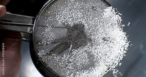 Super slow motion macro of professional artisan baker chef sprinkles sugar icing powder with sieve while making homemade pastries or dessert cake in traditional bakery kitchen.