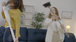 Funny teen girls dancing with broom and vacuum cleaner while cleaning the room