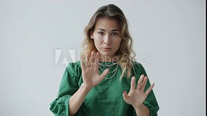 Slow motion of serious young woman touching lips with finger and making calm down hand gesture on white background. People and body language concept.