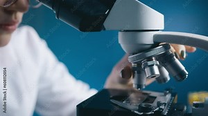 Female studying DNA mutations by looking and rotating microscope in modern medical science laboratory. Microbiologist working with microscope analyzing samples. Scientist working High-Tech Equipment