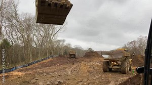 Excavator cab view showing an articulating site truck backing up to get loaded by an excavator