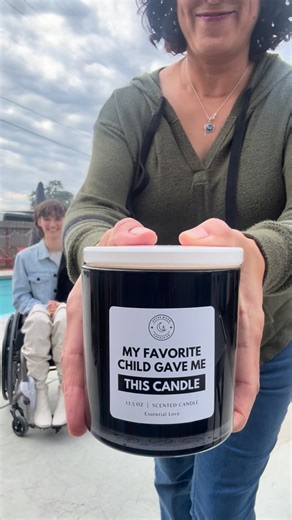 Aly Corvin on Instagram: "Meet my mom… the giver of the DNA.. 🧬 💀🫠 Alt text: a woman sits in her wheelchair and talks to her mom. Her mom shows the camera a candle that says “My favorite child gave me this candle”. The girl in the wheelchair is wearing black leather pants, a white cut-out bodysuit, split dye jean jacket and knee-high white boots. She’s sitting in front of an outdoor swimming pool. Her mom is wearing jeans, tennis shoes and a green hoodie. Words on screen explain that she is p