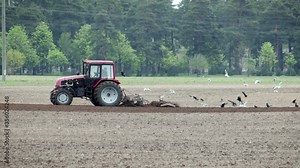 The topic is agriculture. The farmer rides in a tractor and monitors how the tractor performs plowing the land with a trailer plow. Farm and automation using machines