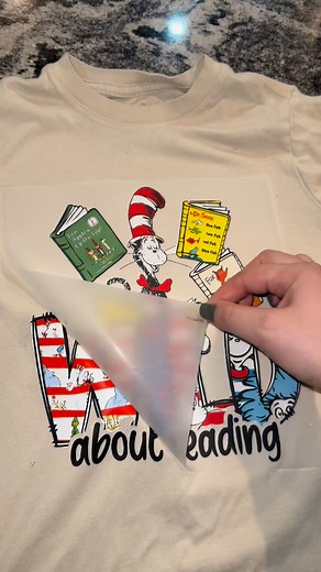 No heat press no problem! Use DTF transfers at home with a household iron. Apply an even amount of pressure for 20 seconds on the entirety of the image. Repeat with parchment paper. Let the shirt cool down completely before lifting evenly from one corner. #DIY #readacrossamerica #diydtf #dtftransfers #shirtmaking #schooldiy #schoolcrafts #athomecrafts #heatpress #heatpressmachine #heatpressvinyl #heatpresstransfers #shirttransfers #shirthack #shirtmaking #diyproject #diyprojects | T-Shirt Upcycl