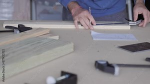 The carpenter measured and marked the plank of wood, following the specifications on the paper with a right angle ruler and pencil.