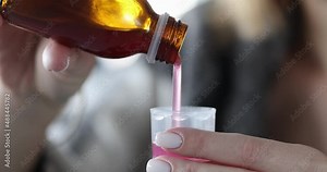 Woman pours cough syrup into measuring cup closeup
