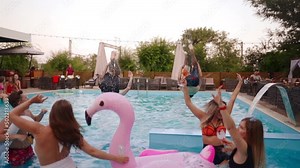 Friends have pool party dancing in private villa swimming pool. Cheerful young people in swimwear jump and dive splashing water in luxury resort. Men and women hanging out in slow motion.