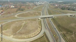 Elevated roads intersecting over flat terrain, with traffic circulating amidst construction areas and nearby urban development