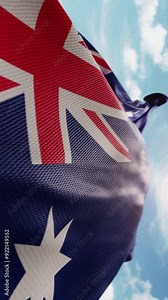 Wavy flag of Australia blowing in the wind in slow motion. Waving colorful Australian flag symbol abstract vertical video background. Sun and blue sky with clouds on a background